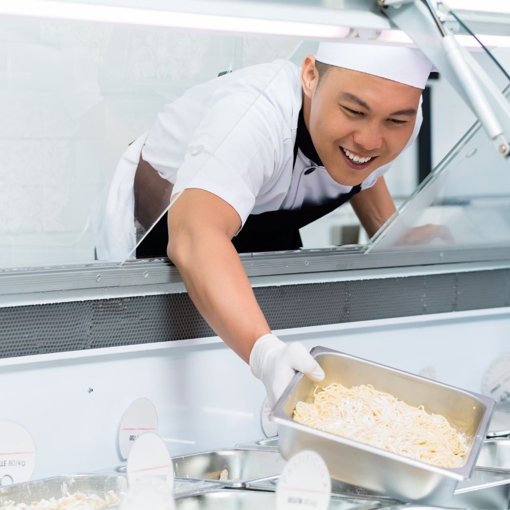 Un chef heureux de placer des crudités sur le comptoir vitrine. Frigo Horeca